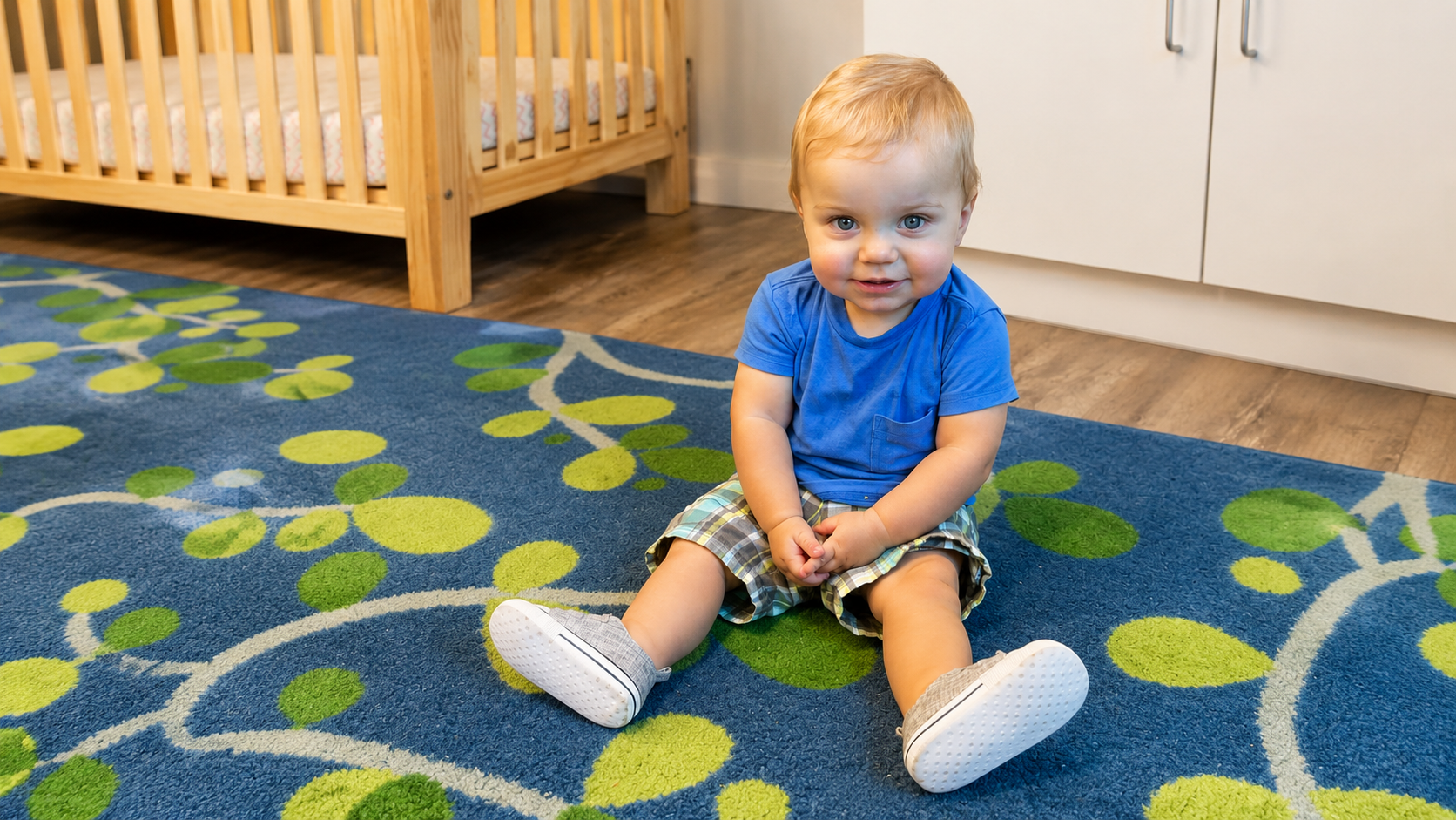 Toddler in a blue shirt smiling while seated on the classroom rug
