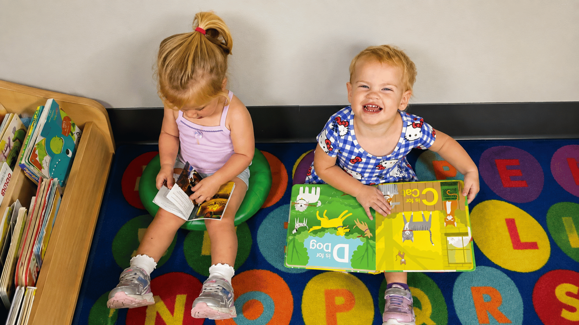 Two toddlers reading picture books on an alphabet rug at KinderKids Learning Center