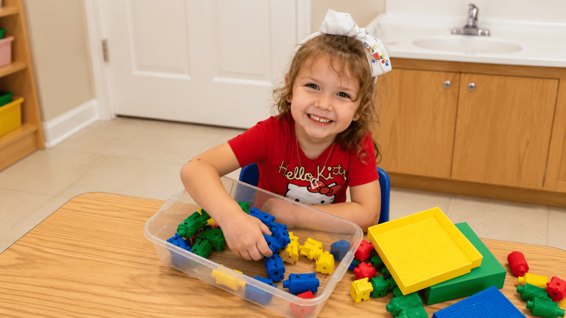A preschooler smiling while building with colorful connecting blocks at KinderKids Learning Center