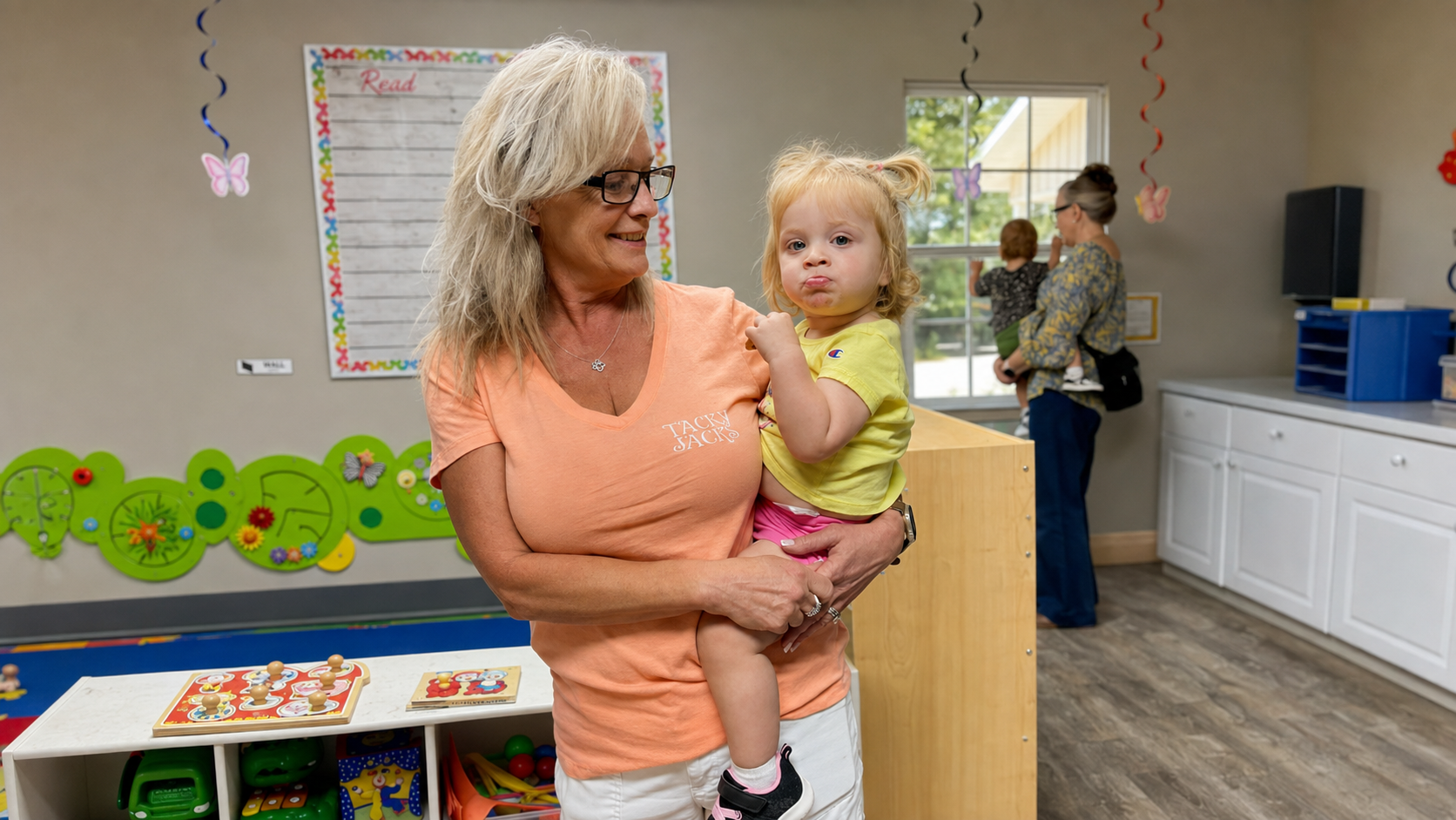 KinderKids teacher holding a toddler during a warm morning drop-off in the classroom