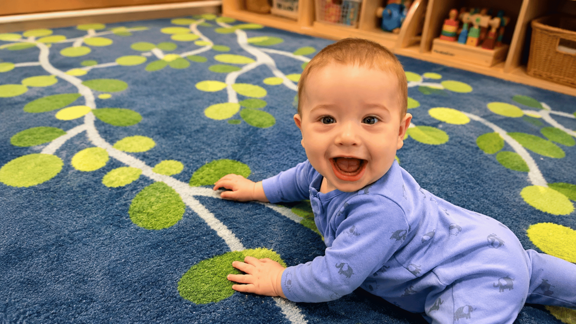 Smiling infant crawling on a leafy blue classroom rug